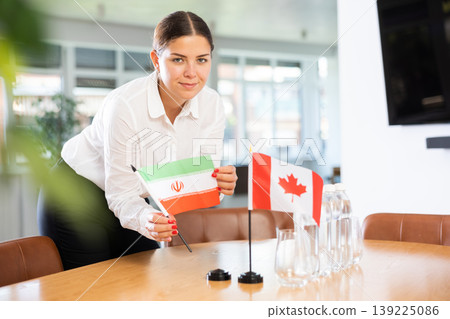 Young woman puts flags of Iran and Canada on table in office 139225086