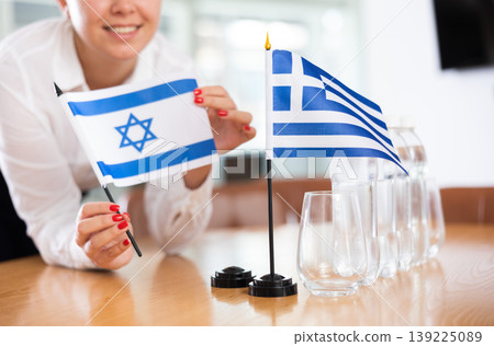 Young woman putting flags of Israel and Greece on table in office 139225089