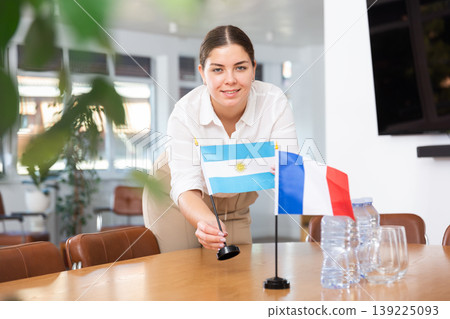 Positive young woman putting flag of Argentina on the table with flag of France in conference room Positive young woman putting flag of Argentina on the table with flag of France in conference room 139225093