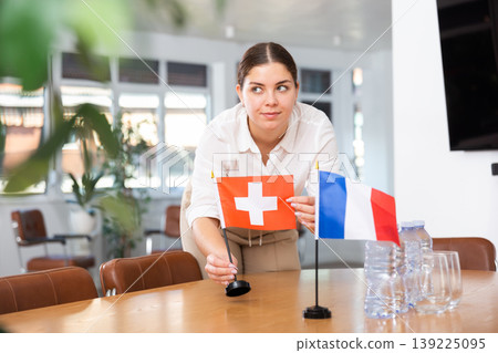 Employee of delegation prepares negotiating table - sets up flag of Switzerland and France Employee of delegation prepares negotiating table - sets up flag of Switzerland and France 139225095