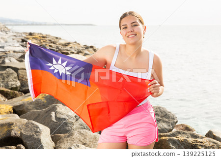 Enjoying vacation in Taiwan. Young woman with national Taiwanese flag on the seashore on sunny day 139225125
