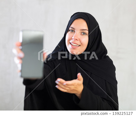 Smiling young woman dressed in traditional islamic clothes displaying brand new smartphone 139225127