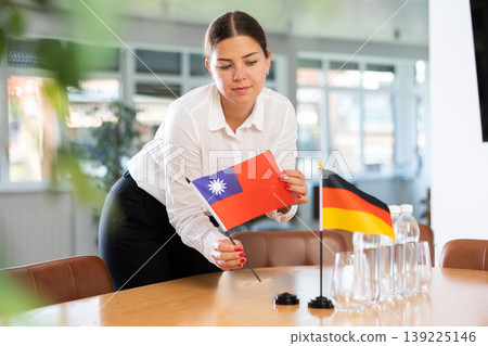 Positive young woman putting little flag of Taiwan on table next to the flag of Germany Positive young woman putting little flag of Taiwan on table next to the flag of Germany 139225146