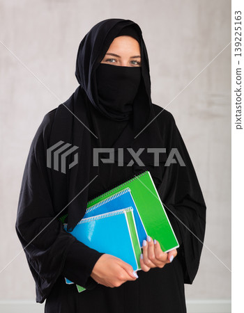 girl with face covered with burka holds lot of thick notebooks. foreign 139225163
