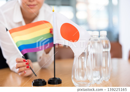 Rainbow flag and flag of Japan in female hands on negotiating table 139225165