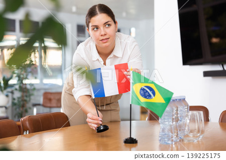 Young female assistant putting up brazilian and french flags on table for international negotiations Young female assistant putting up brazilian and french flags on table for international negotiations 139225175