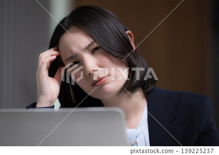 A portrait of a woman exhausted from working overtime on her computer, striking a troubled pose due to a migraine, representing the struggles of overwork and the pain of headaches. A portrait of a woman exhausted from working overtime on her computer, striking a troubled pose due to a migraine, representing the struggles of overwork and the pain of headaches. 139225237