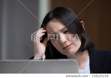 A portrait of a woman exhausted from working overtime on her computer, striking a troubled pose due to a migraine, representing the struggles of overwork and the pain of headaches. A portrait of a woman exhausted from working overtime on her computer, striking a troubled pose due to a migraine, representing the struggles of overwork and the pain of headaches. 139225238