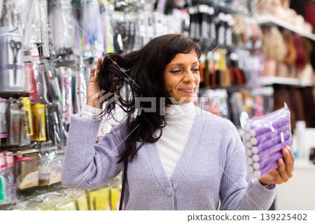 Smiling latina choosing hair rollers in store 139225402