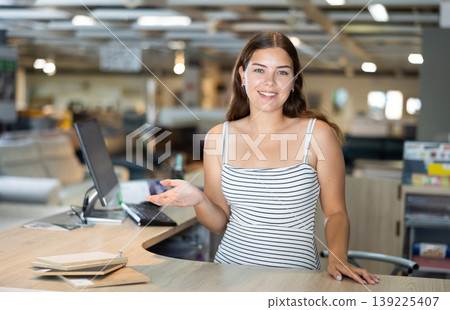 Portrait of positive female consultant in a furniture store at reception desk 139225407