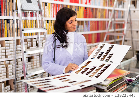 Hispanic woman choosing dye for hair coloring in cosmetics store Hispanic woman choosing dye for hair coloring in cosmetics store 139225445