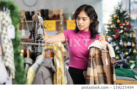 Woman chooses and tries coat in clothing store before Christmas Woman chooses and tries coat in clothing store before Christmas 139225494