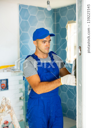 Industrial worker, handyman in blue construction overalls installing tiles on bathroom walls 139225545