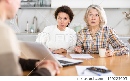 Two women sitting at the kitchen-table face to face with male agent 139225605