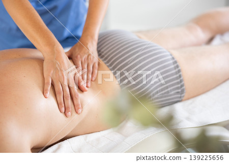 Female masseur works out back and lower back area of male client. Close-up 139225656