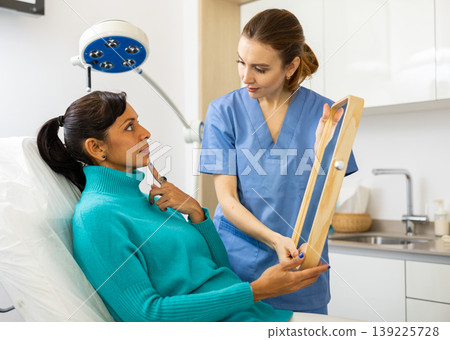 Latin woman holding mirror during cosmetologist's examination Latin woman holding mirror during cosmetologist's examination 139225728