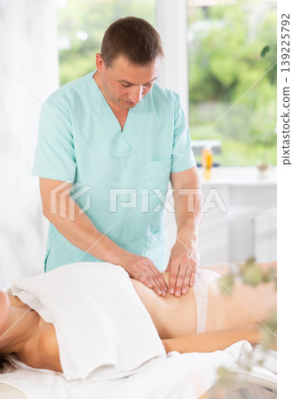 Male masseur performs stroking and rubbing during spa procedure in abdominal area for female client Male masseur performs stroking and rubbing during spa procedure in abdominal area for female client 139225792