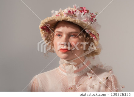 Young woman models elaborate flower hat and vintage-inspired sheer top in a bright studio Young woman models elaborate flower hat and vintage-inspired sheer top in a bright studio 139226335