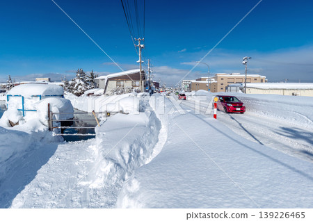 雪鄉的日常生活：陽光明媚的冬日，一條積雪覆蓋的道路。堆積的積雪正被傾倒進左側可見的河流中。 139226465