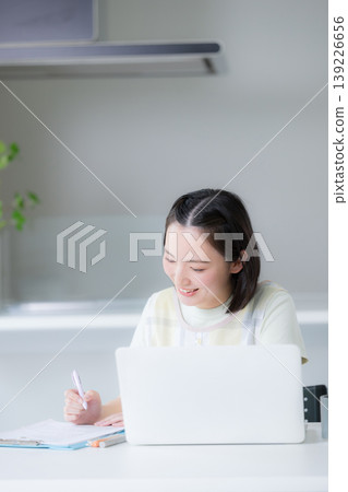 一位微笑的女士在餐廳裡用筆記型電腦工作;一位遠距工作者,在家工作或學習資格證書,例如管理家庭財務。 一位微笑的女士在餐廳裡用筆記型電腦工作;一位遠距工作者,在家工作或學習資格證書,例如管理家庭財務。 139226656