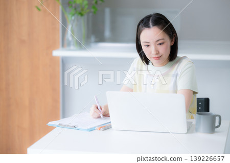 一位微笑的女士在餐廳裡用筆記型電腦工作;一位遠距工作者,在家工作或學習資格證書,例如管理家庭財務。 一位微笑的女士在餐廳裡用筆記型電腦工作;一位遠距工作者,在家工作或學習資格證書,例如管理家庭財務。 139226657
