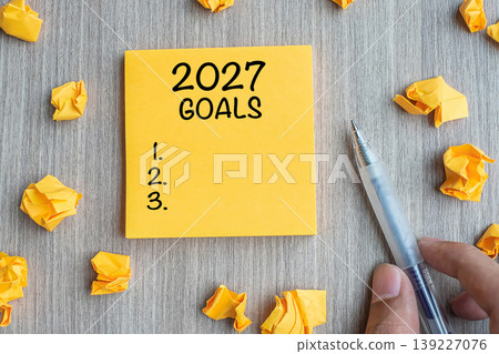2027 Goal word on yellow note with Businessman holding pen and crumbled paper on wooden table background. New Year New Start, Resolutions, Strategy, mission concept 2027 Goal word on yellow note with Businessman holding pen and crumbled paper on wooden table background. New Year New Start, Resolutions, Strategy, mission concept 139227076