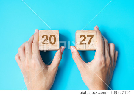 hand holding wooden cube block with 2027 text on blue background. Resolution, plan, review, goal, start and New Year holiday concepts hand holding wooden cube block with 2027 text on blue background. Resolution, plan, review, goal, start and New Year holiday concepts 139227105