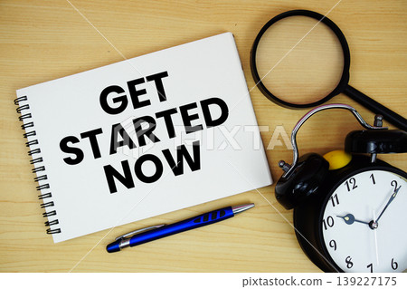 Get Started Now text written on notepad with alarm clock and magnifying glass flat lay on wooden background 139227175