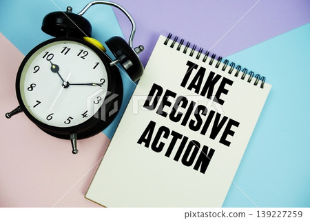 Take Decisive Action text written on notepad with alarm clock flat lay on multicolor pastel background 139227259