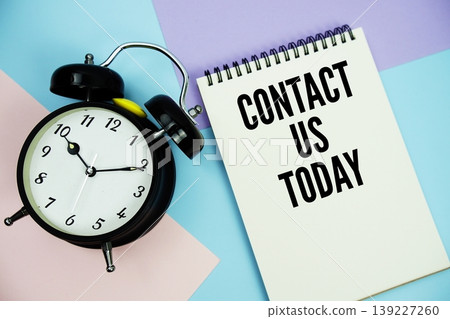 Contact Us Today text written on notepad with alarm clock flat lay on multicolor pastel background 139227260