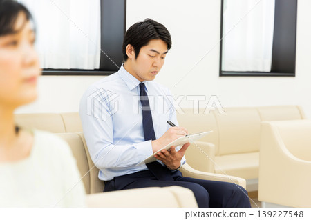 一位商務人士在候診室填寫醫療問卷。 一位商務人士在候診室填寫醫療問卷。 139227548