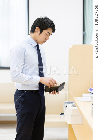 一位商人正在醫院前台付款。 一位商人正在醫院前台付款。 139227559