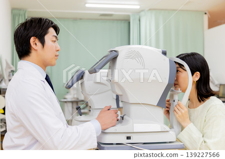 A scene in an ophthalmologist's office showing a doctor performing a vision test on a female patient. A scene in an ophthalmologist's office showing a doctor performing a vision test on a female patient. 139227566