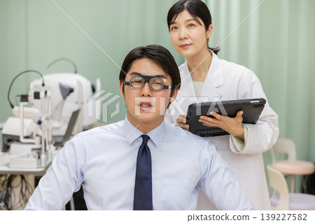 A male patient undergoing an eye exam and a female doctor recording the results on a tablet. A male patient undergoing an eye exam and a female doctor recording the results on a tablet. 139227582
