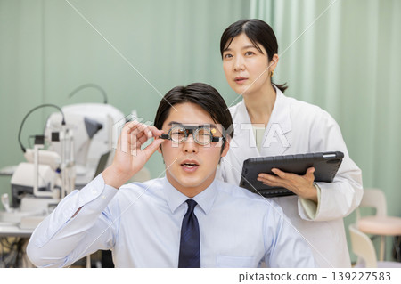 A male patient undergoing an eye exam and a female doctor recording the results on a tablet. A male patient undergoing an eye exam and a female doctor recording the results on a tablet. 139227583