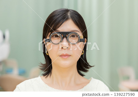 一位女士正在接受眼科檢查,並戴著試戴鏡架的正面肖像。 一位女士正在接受眼科檢查,並戴著試戴鏡架的正面肖像。 139227590