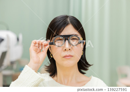 Front view portrait of a woman undergoing an eye exam with a trial frame. Front view portrait of a woman undergoing an eye exam with a trial frame. 139227591