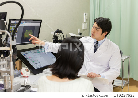 A scene of an ophthalmologist explaining test results to a patient during a consultation (the monitor is a test screen). A scene of an ophthalmologist explaining test results to a patient during a consultation (the monitor is a test screen). 139227622