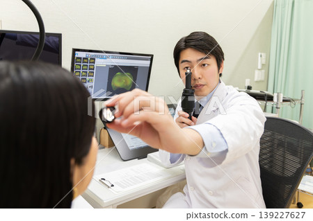 A scene from a medical examination where an ophthalmologist examines a female patient's eyes using a penlight (the monitor is a test screen). A scene from a medical examination where an ophthalmologist examines a female patient's eyes using a penlight (the monitor is a test screen). 139227627