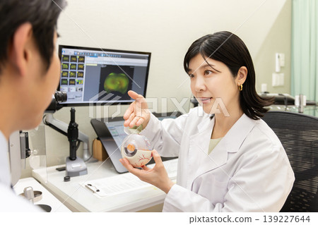 眼科醫生使用眼球模型講解檢查方法;視力和眼部健康諮詢(顯示器顯示測試螢幕)。 眼科醫生使用眼球模型講解檢查方法;視力和眼部健康諮詢(顯示器顯示測試螢幕)。 139227644