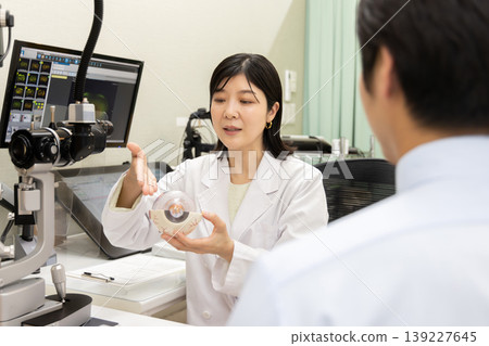 An ophthalmologist explains an examination using an eyeball model; vision and eye health counseling (the monitor shows a test screen). An ophthalmologist explains an examination using an eyeball model; vision and eye health counseling (the monitor shows a test screen). 139227645
