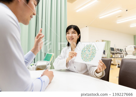 A patient correctly answers a color vision test, and the ophthalmologist smiles – a reassuring examination scene. A patient correctly answers a color vision test, and the ophthalmologist smiles – a reassuring examination scene. 139227666