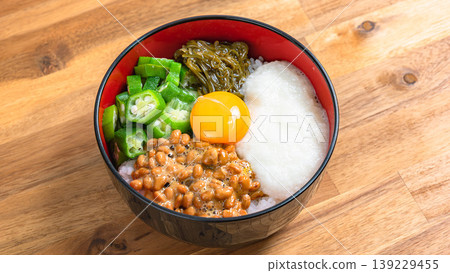 Sticky Rice Bowl: Rice topped with natto, okra, grated yam, mekabu seaweed, and egg yolk, against a wood grain background. Sticky Rice Bowl: Rice topped with natto, okra, grated yam, mekabu seaweed, and egg yolk, against a wood grain background. 139229455