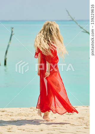 A beautiful tanned girl is wearing in red cape fun on the personal beach of the villa on a sunny day in the Maldives, she is happy and posing A beautiful tanned girl is wearing in red cape fun on the personal beach of the villa on a sunny day in the Maldives, she is happy and posing 139229616