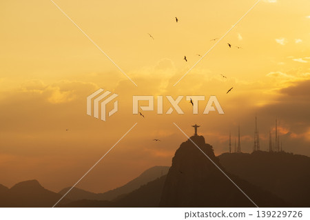 Peaceful sunset over Christ Redeemer statue on mountain in Rio de Janeiro Brazil with birds flying in golden sky Peaceful sunset over Christ Redeemer statue on mountain in Rio de Janeiro Brazil with birds flying in golden sky 139229726
