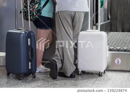 Airport passengers with their two wheeled suitcases standing near the check-in baggage belt 139229874