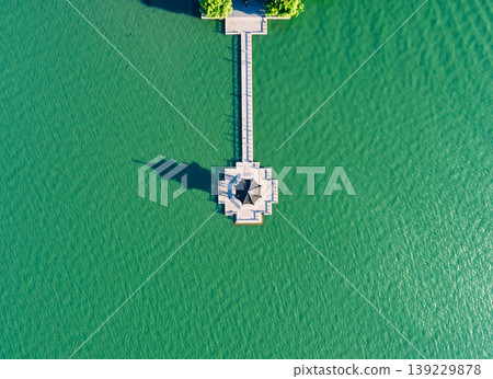 Aerial top down view of unique hexagonal pavilion at the end of a long white pier extending into vibrant green water Aerial top down view of unique hexagonal pavilion at the end of a long white pier extending into vibrant green water 139229878
