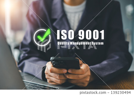 Close-up of a business professional using a smartphone with ISO 9001 quality management system concept in a modern office. Close-up of a business professional using a smartphone with ISO 9001 quality management system concept in a modern office. 139230494