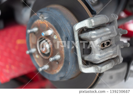 Close up of car brake caliper and disc rotor during maintenance showing automotive repair inspection metal components and vehicle safety system in garage 139230687
