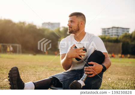 Conception of returning to the sport, sitting. Strong amputee man with prosthesis is with soccer ball on the field 139230828